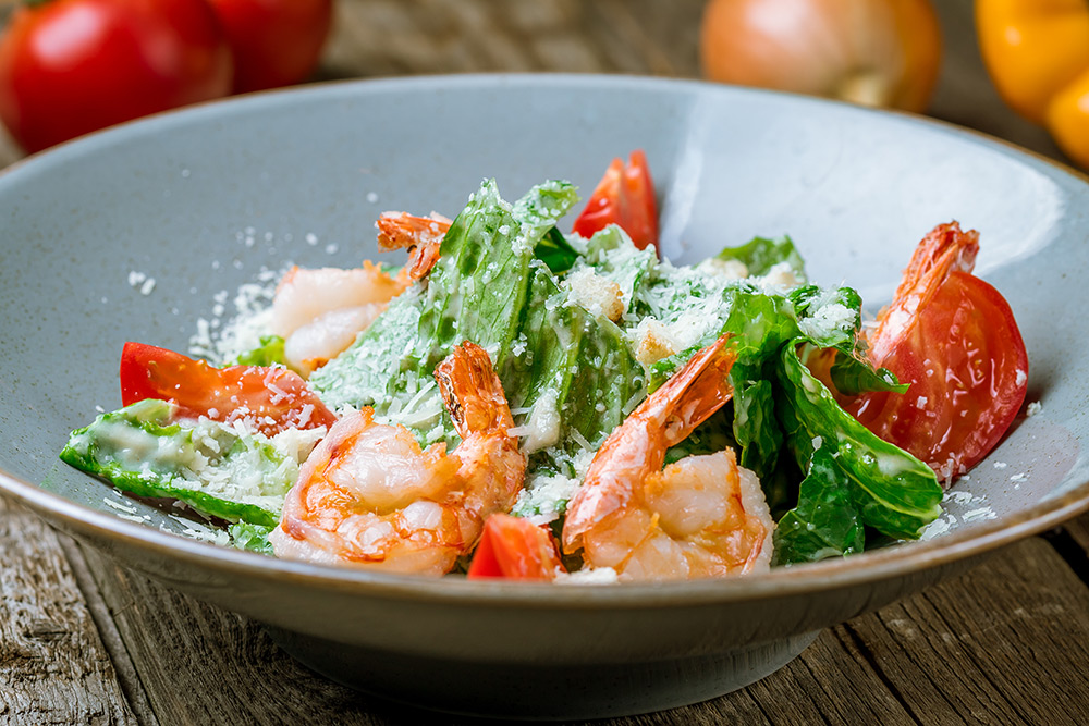 Caesar Salad per gli amanti del pesce: gamberi, pomodori, foglie di basilico e dressing caesar